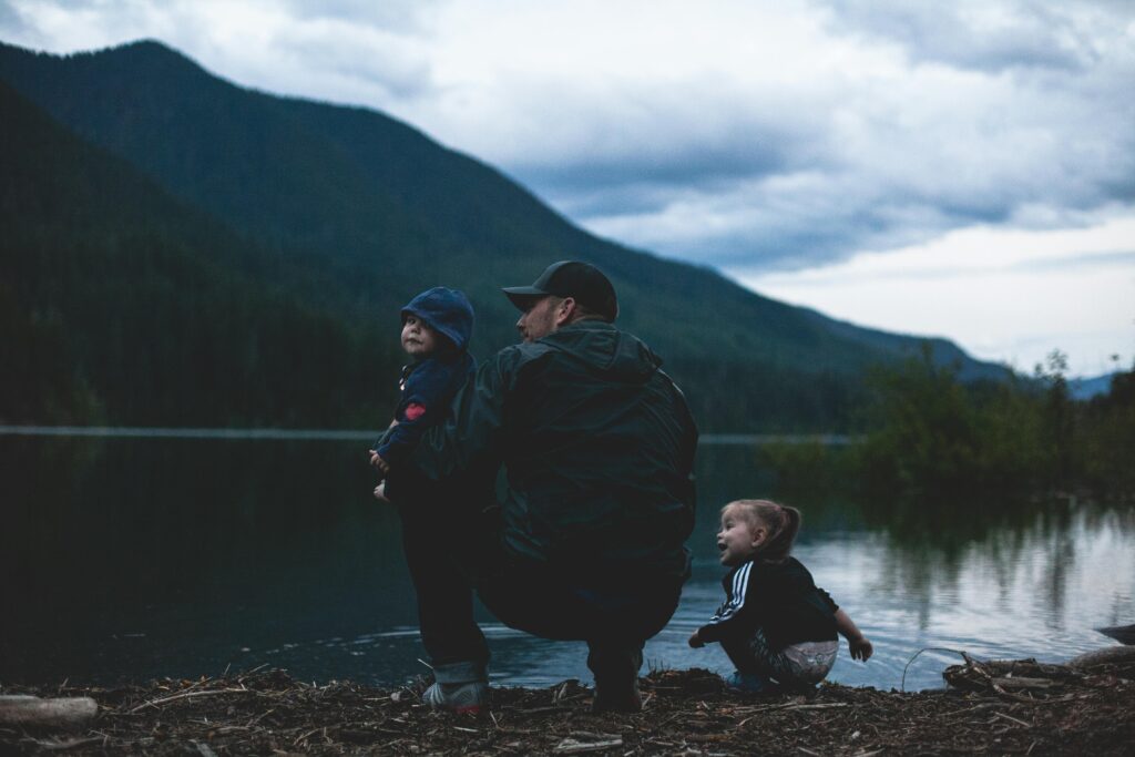 Father and children enjoy a serene moment by a lakeside with mountains.