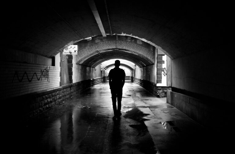 A person walking alone through a dimly lit tunnel, captured in black and white.