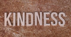 Wooden letters spelling 'Kindness' on a textured stone background, conveying a positive message.